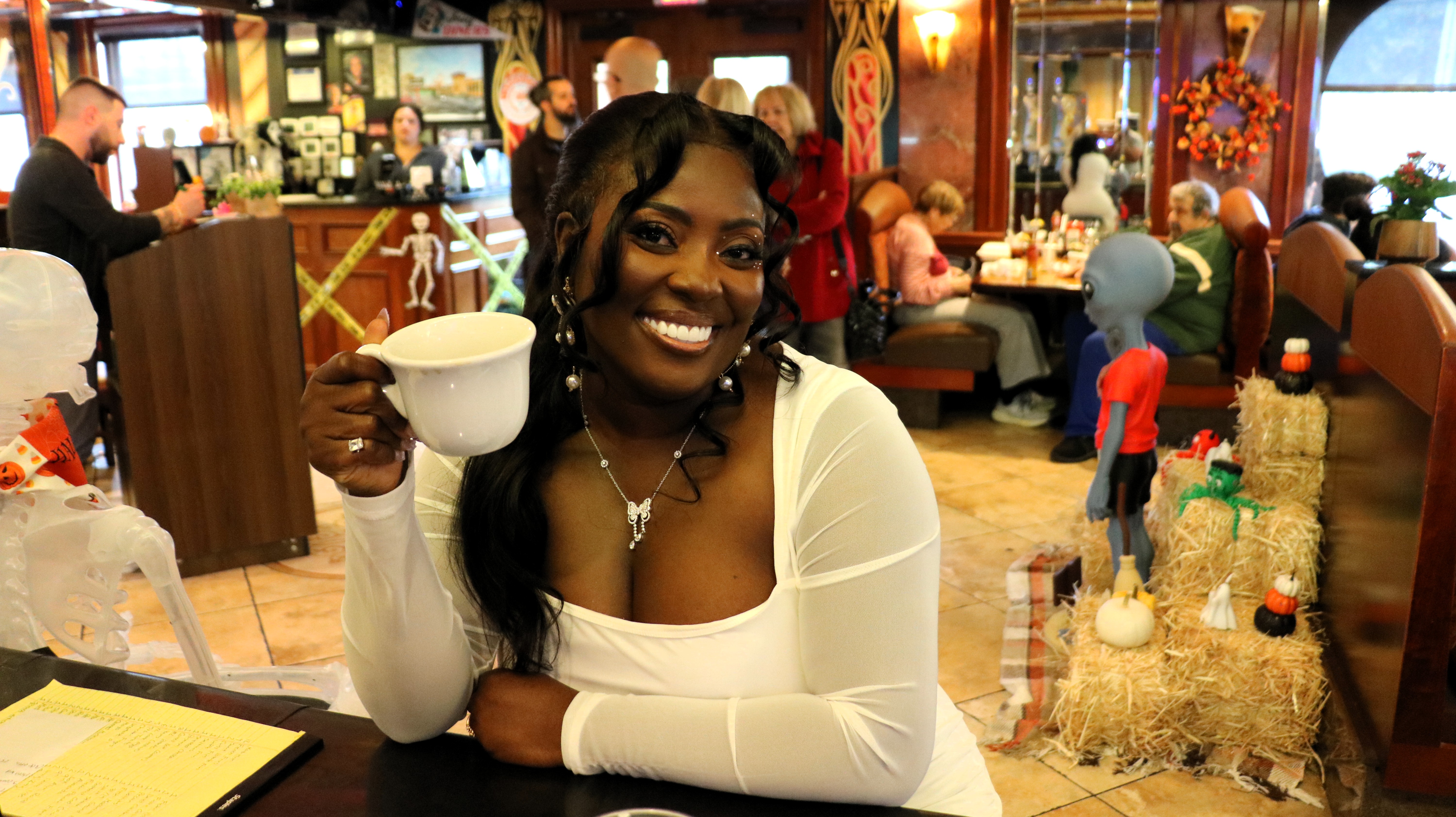 Lynn smiling and raising a cup, inviting you to join her.